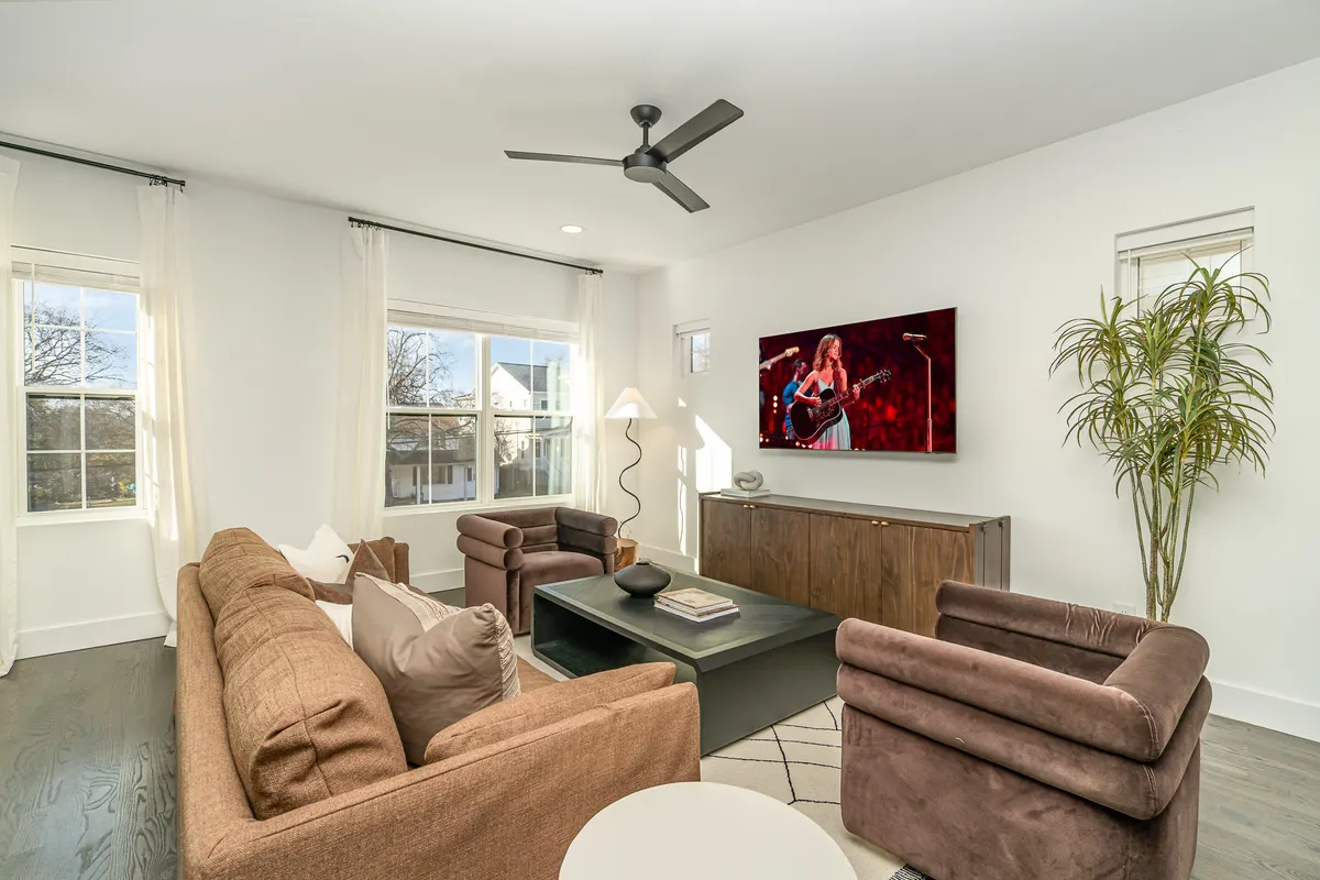 The image showcases a stylish and inviting living room featuring a plush sofa, large television, chic coffee table, modern floor lamp, and vibrant greenery, creating a space perfect for relaxation and social gatherings. The layout and decor suggest a contemporary comfort ideal for unwinding or spending time with friends and family.