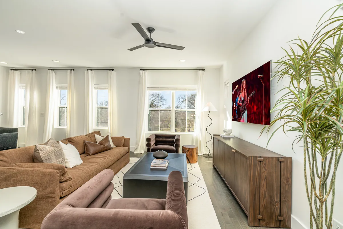 This image features a large sectional sofa arranged around a modern coffee table, complemented by a television showcasing artwork, a potted plant, and a floor lamp. The room is spacious, inviting, and designed for comfort and togetherness—perfect for movie nights and relaxed gatherings.