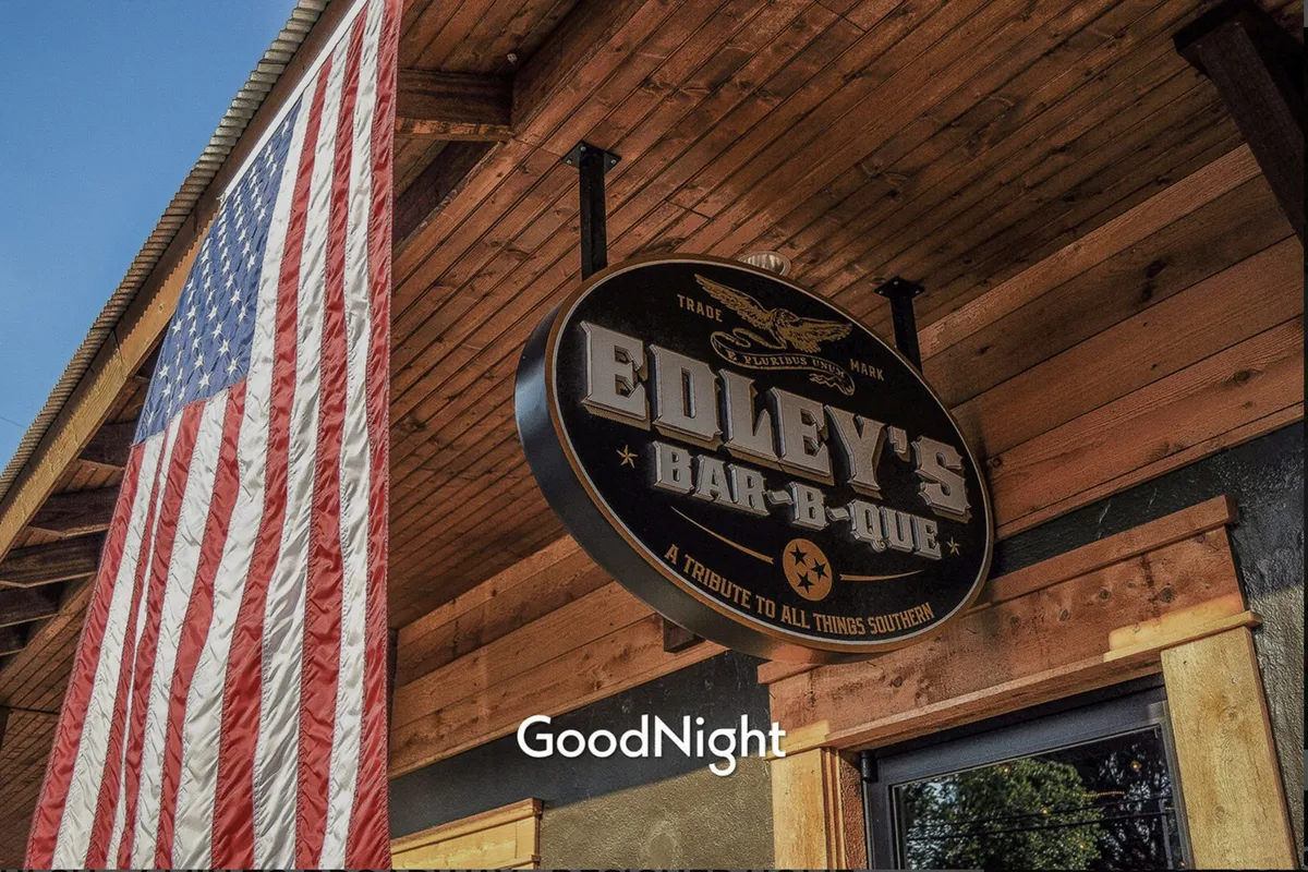 Edley’s Bar-B-Que’s welcoming exterior, featuring its iconic sign and American flag, radiates a friendly, communal vibe. The setting hints at local dining experiences and neighborhood gatherings.