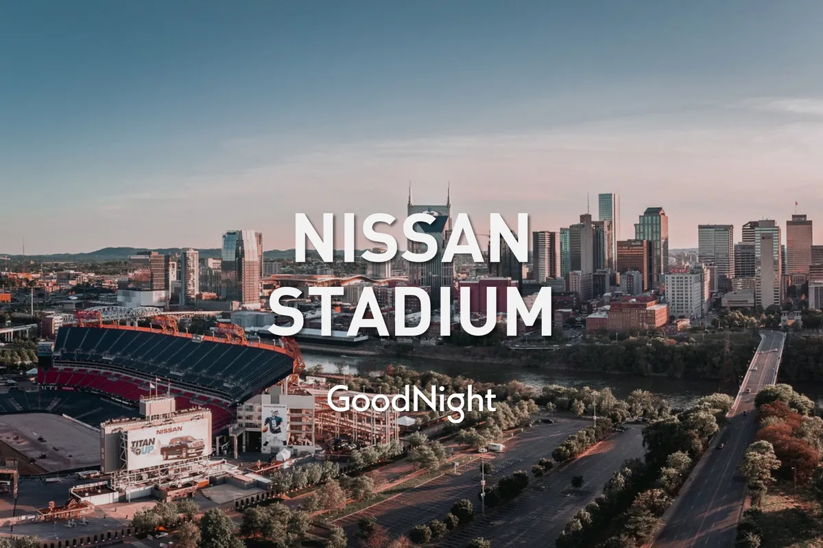 A panoramic view of Nissan Stadium across the river with the Nashville skyline in the background. The tranquil scene highlights the proximity to major entertainment venues and the picturesque setting along the water.