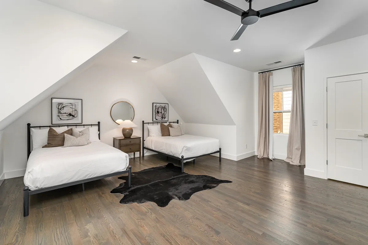 A calm, comfortable bedroom featuring two beds with crisp white linens, elegant black-and-white artwork, a circular mirror, and a soft cowhide rug. The decor is soothing and adaptable, suiting a range of guests.