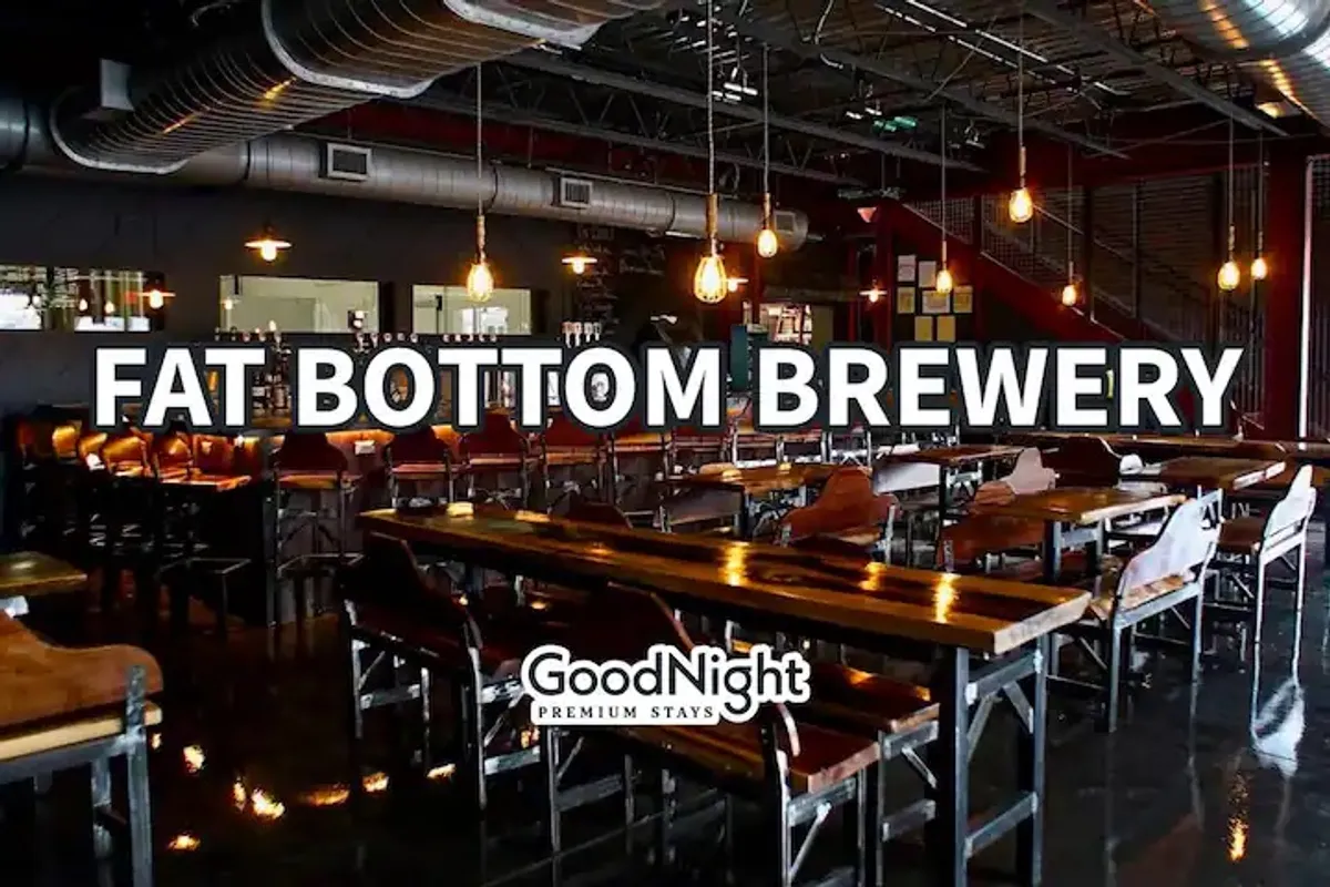 An energetic interior scene with long wooden tables, bar seating, industrial lighting, and an exposed brick wall. Groups are seen socializing and dining, capturing the communal, family-oriented spirit of a local brewery or café.